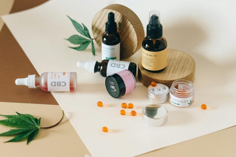 Assortment of CBD products including oils, salve, capsules, and face serum displayed with hemp leaves and gel capsules